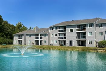 A fountain in a lake in front of an apartment building